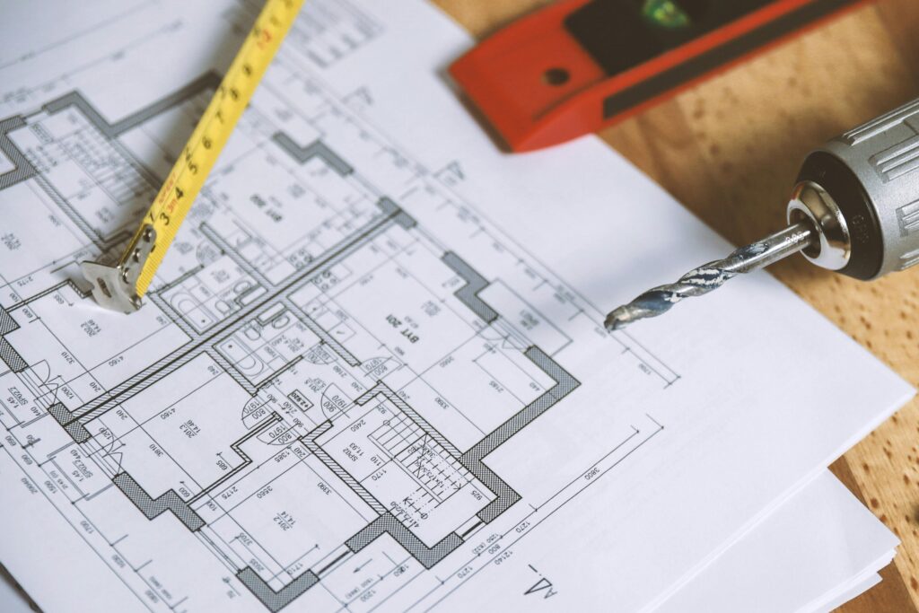 Close-up of construction blueprint with tools like drill and screws on a wooden table.